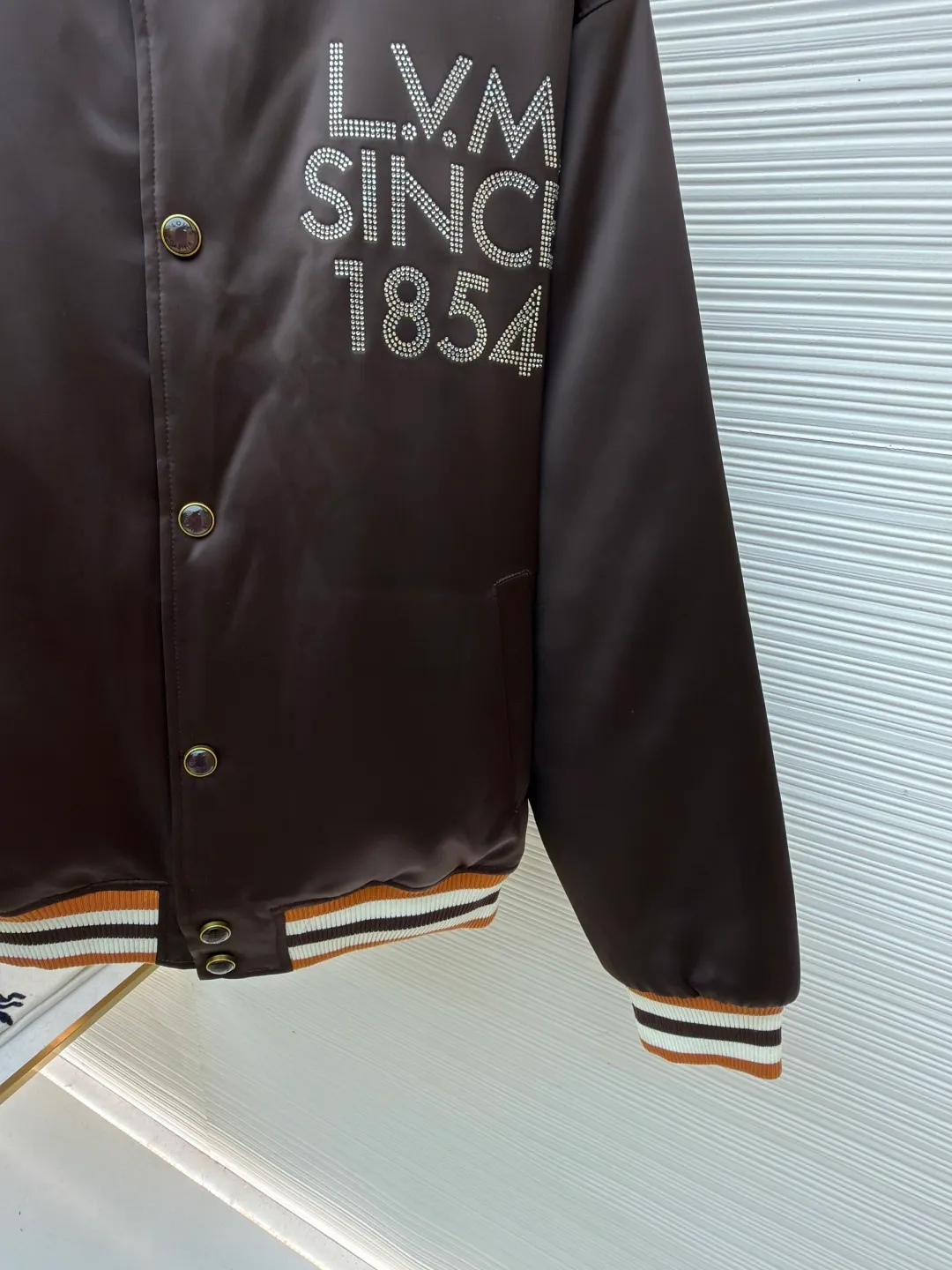 LOUIS VUITTON decorative flight jacket ●Original version: 30,000 purchased and developed ●Item number: 1682285-B90 ●Fabric: cotton fabric ●Technology: patch production ●Color: brown ●Version: fitted version ●Weight: about 1085 grams ●Size: 46-48-50-52 ●Description: The main body of this Louis Vuitton satin baseball jacket is made of high-density matte satin fabric, which has been treated with anti-wrinkle shaping technology. The fabric has a strong drape and is not easy to wrinkle. The dark brown background color is prepared by precision dyeing and finishing technology, giving it a rich color and high-end texture. The "L.V.M SINCE 1854" logo on the left chest is made with hot-drilling technology. High-quality rhinestones are used for precise hot-pasting in different areas. The diamond surface is shiny and strong and will not fall off easily. The ribbed splicing of the collar, cuffs and hem is a three-color contrasting design. It is woven with high-elastic knitted yarn, which will not easily loosen and deform after long-term wear. The placket is equipped with custom-made metal snaps. The hardware is thick and anti-oxidation. The overall style is loose and off-shoulder. The splicing is covered with blind stitching technology, and the wiring is smooth and traceless. Every craft detail follows the brand's luxury product production standards, taking into account both design and wearing comfort. The overall wiring is straight and delicate, the fabric is comfortable and soft, and the color is consistent without color difference. It can be matched with the same style to create a fashionable look and control various occasions. Customized accessories, complete with three standards, same style for men and women!